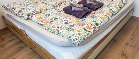 A single bed with a floral bedspread, two purple towels, and a wooden headboard.