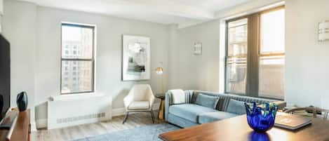 A modern living room with a wooden dining table, a blue sofa, and a white armchair.