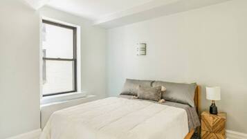 A bedroom with a bed, a window, a nightstand, and a wall-mounted light fixture.