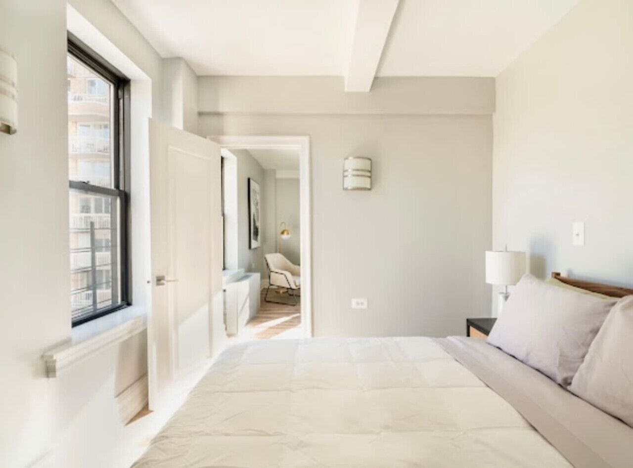 A bedroom with a large bed, a nightstand, a lamp, and a view of a bathroom through an open door.