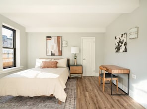 Um quarto com uma cama, uma mesa de cabeceira, uma mesa e uma porta.