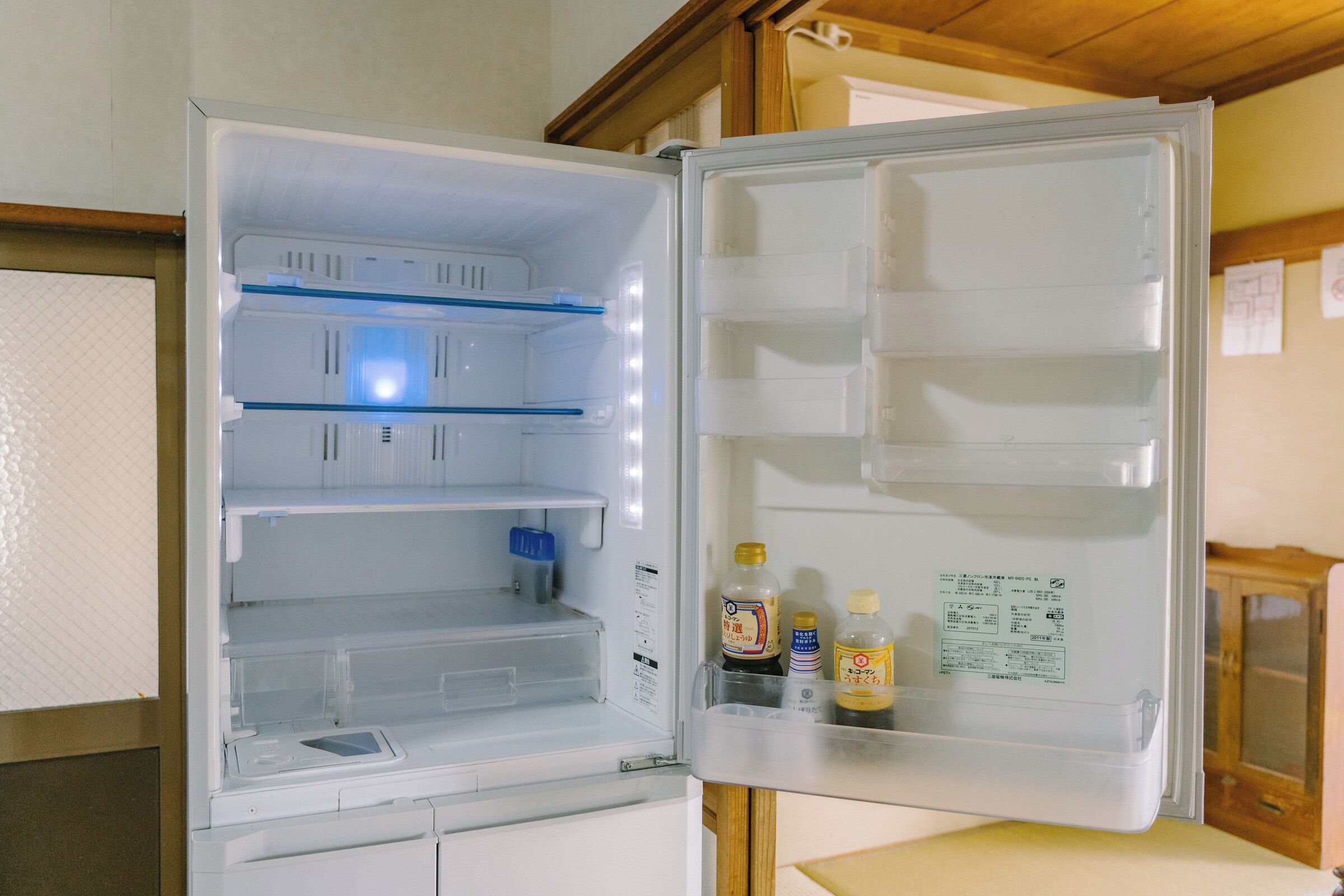 Un réfrigérateur ouvert, doté de plusieurs étagères et compartiments, d’un distributeur d’eau et de quelques bouteilles.