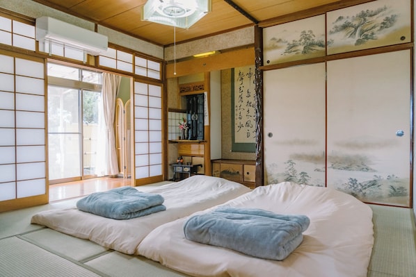 A traditional Japanese-style room with tatami flooring, two beds with blue blankets, sliding doors with artwork, and a ceiling fan.