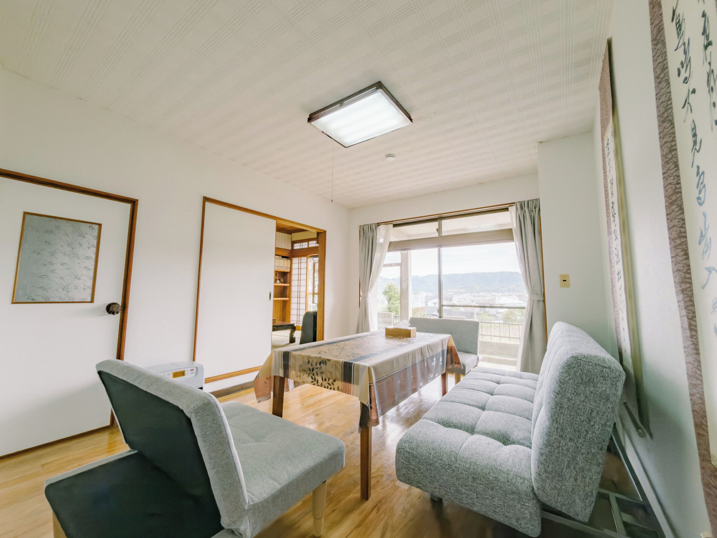 Una habitació amb taula de dinar, dues cadires, un sofà, un armari de fusta i vistes per la finestra.