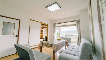 Una habitació amb taula de dinar, dues cadires, un sofà, un armari de fusta i vistes per la finestra.