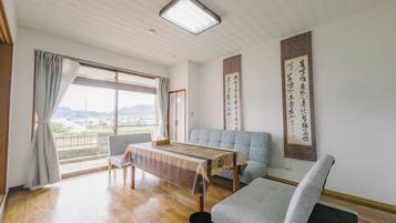 A spacious room with a wooden floor, a sofa, a table, and a view through a large window.