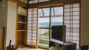 Ein traditioneller japanischer Raum mit Tatami-Bodenbelag, einer Schiebetür mit Aussicht, einem Fernseher und einem Bücherregal.