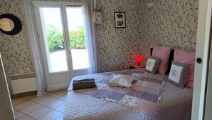 A bedroom with a bed, a bedside lamp, a radiator, a window, and a door. - Just 30 minutes from the river, a countryside vacation rental with a view of Mont Ventoux! (Piolenc)