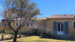 A single-story building with a tiled roof, a front door with a small porch, and a tree with pink flowers in the foreground. - Just 30 minutes from the river, a countryside vacation rental with a view of Mont Ventoux! (Piolenc)