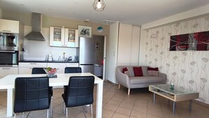 A modern kitchen with built-in appliances, a dining area with a white table and black chairs, and a living area with a sofa and a glass coffee table. - Just 30 minutes from the river, a countryside vacation rental with a view of Mont Ventoux! (Piolenc)