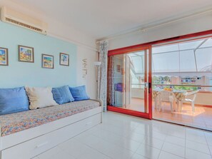Una habitación con sofá, una mesa de comedor con sillas, un ventanal corredero a un espacio exterior y aire acondicionado instalado en la pared.