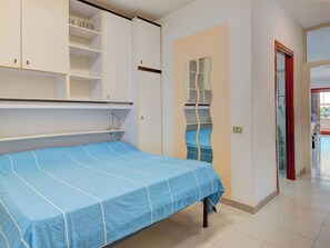 Ein Schlafzimmer mit einem Bett, weißen Schränken, einem Spiegel und einer Tür zu einem weiteren Raum.