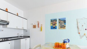 Cozinha com armários brancos, bancada preta e painel de azulejos. Há uma mesa de jantar com toalha amarela e copos laranja.