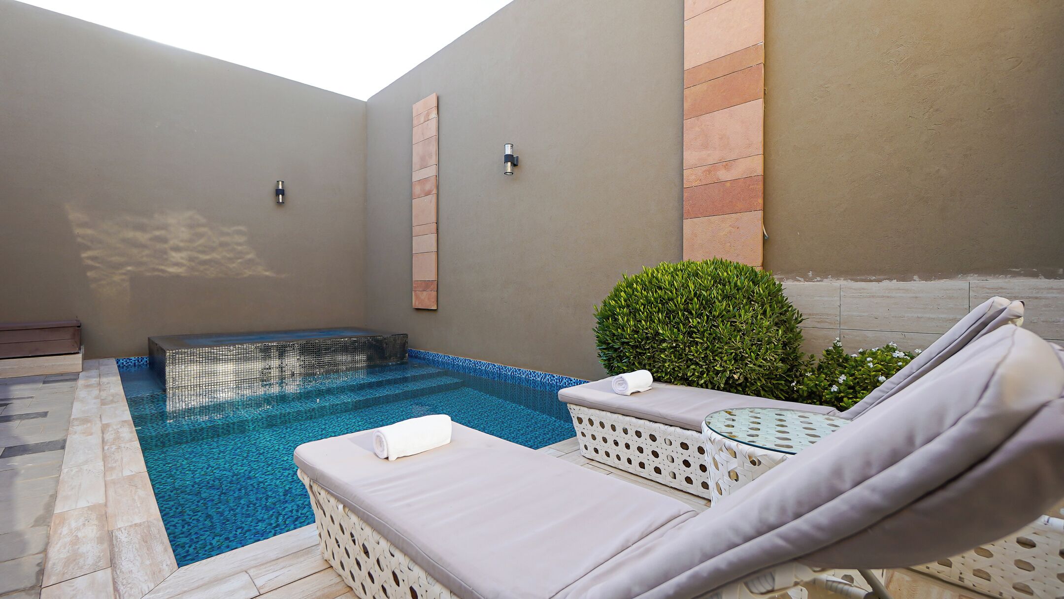 Un espace piscine avec des chaises longues et un petit jacuzzi.