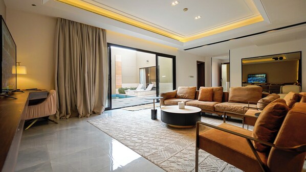 Habitación de hotel moderna con sofá, una mesita de centro, televisor y vista al área de la piscina.