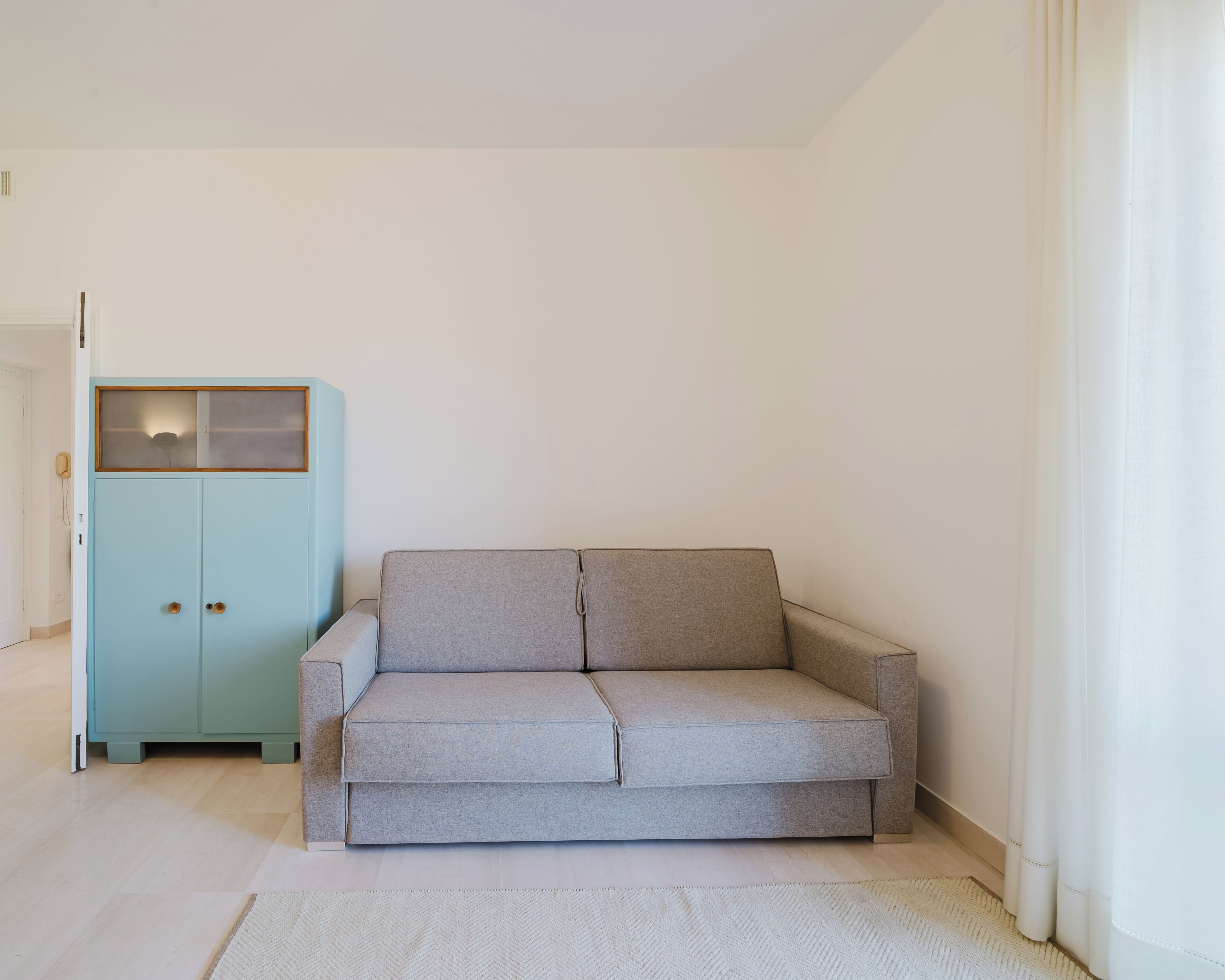 Une pièce avec un meuble bleu clair, un canapé gris et un tapis blanc.