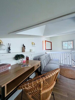 Una sala de estar moderna con un escritorio de madera, un sofá gris, una silla de mimbre y una ventana con vistas.