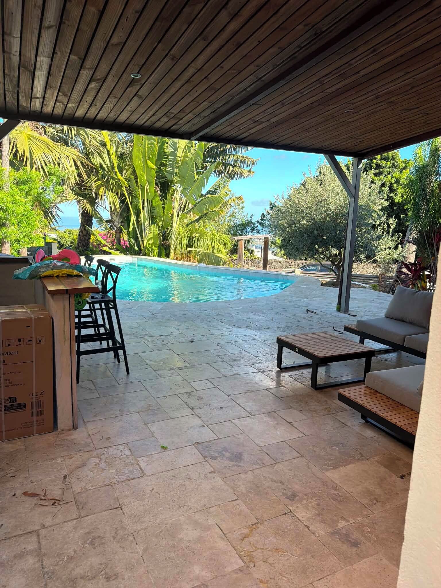 An outdoor pool area with a covered patio, seating, and a view of the ocean.
