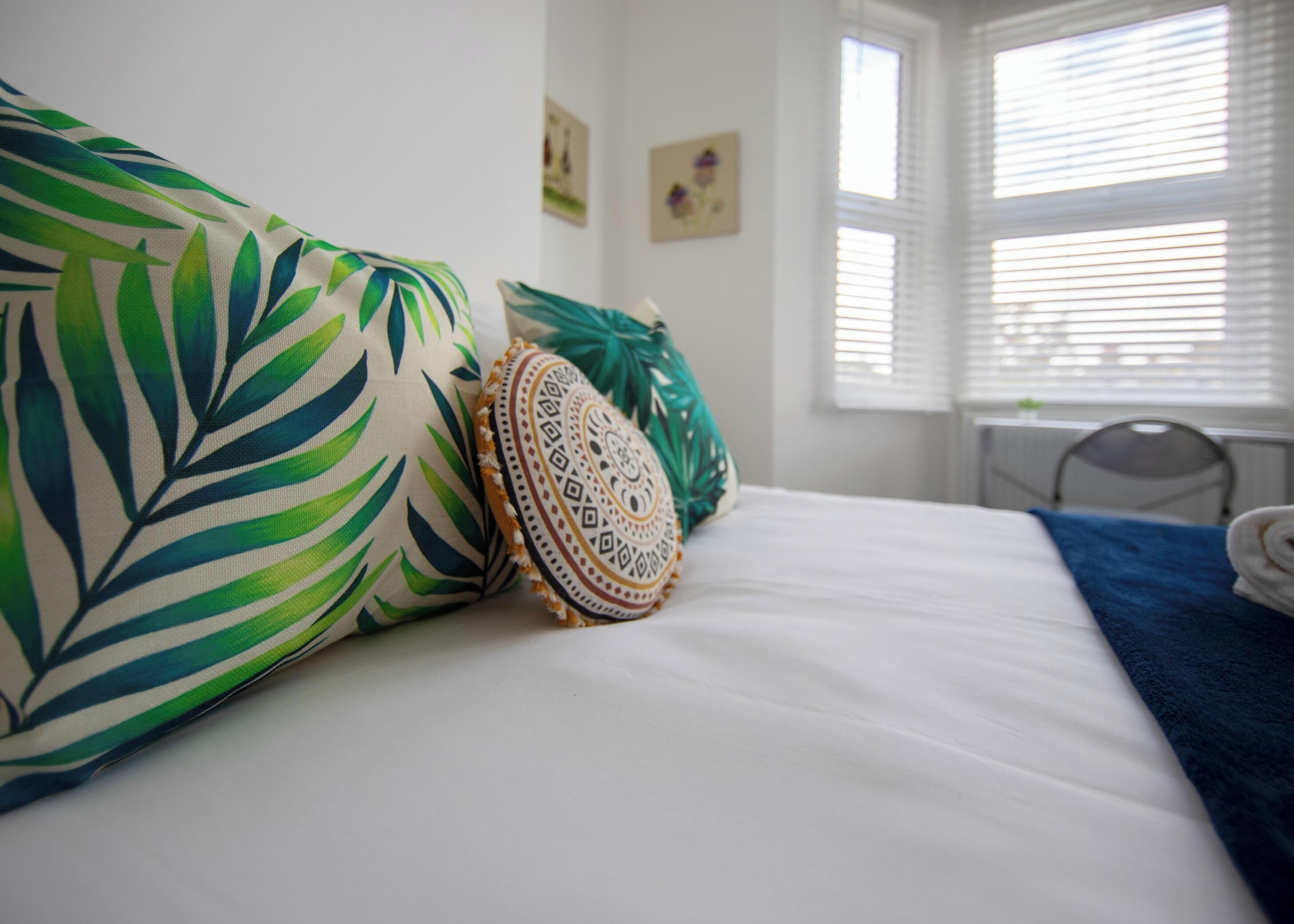 A bed with white bedding, a blue blanket, and decorative pillows with leaf patterns.