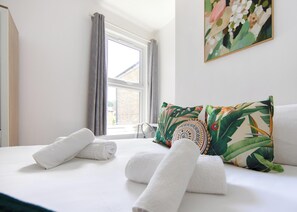 A hotel room with a bed, pillows, and a window. - Spacious 4BR Home Near Elizabeth Line (London)
