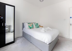 A bedroom with a bed, a large mirror, and a door. - Spacious 4BR Home Near Elizabeth Line  (London)