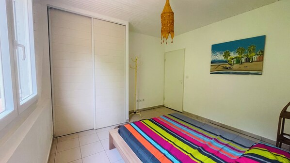 A bedroom with a striped bedspread, a painting on the wall, and a closet.