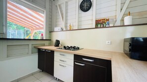 A kitchen with a gas stove, a kettle, and a microwave. There is a window with a view of greenery outside. - Villa Les Alpinias: A Serene Oasis with a Private Pool (Petit-Bourg)