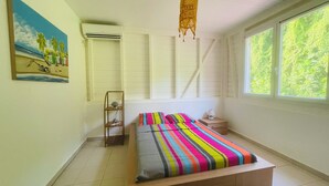 Une chambre à coucher avec un lit, une table de chevet, une lampe, une fenêtre donnant sur un paysage verdoyant et un tableau accroché au mur.