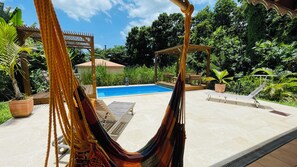 A hammock, a pool, and a patio area with potted plants and a pergola.