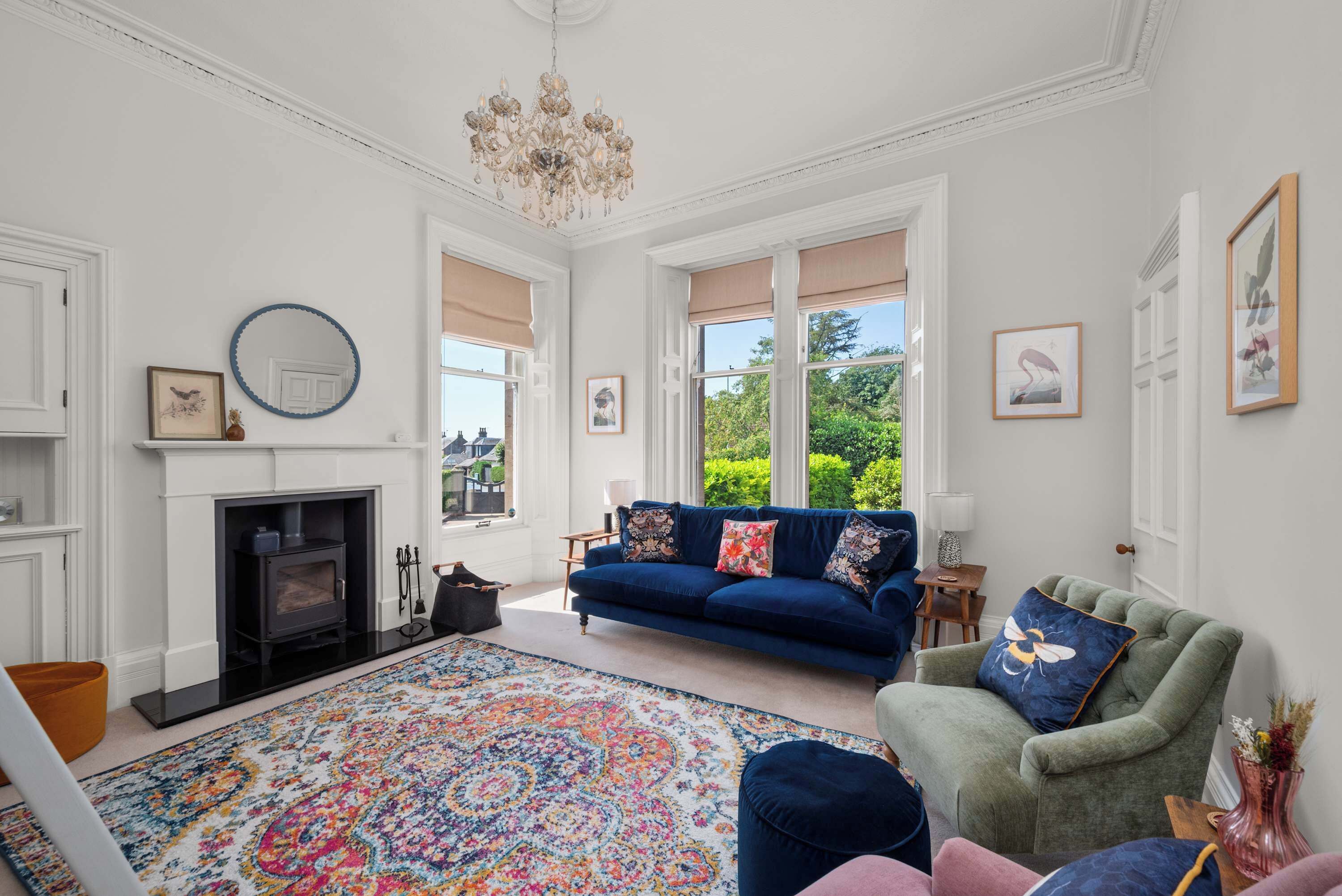 A living room with a fireplace, a blue sofa, a green armchair, and a colorful rug.
