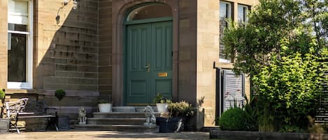 Un edificio histórico con una puerta verde, escalones de piedra y un jardín.