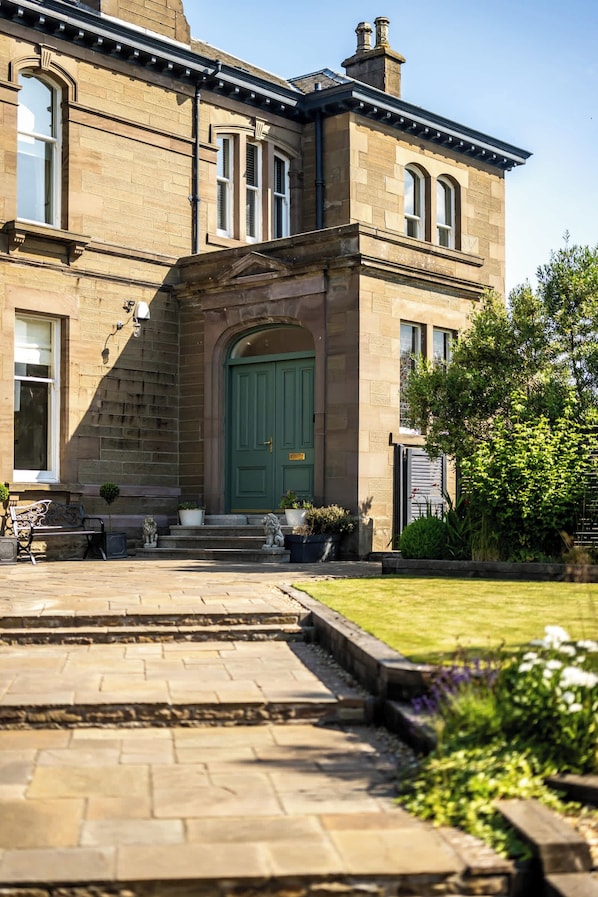 A historic building with a green door, stone steps, and a garden.