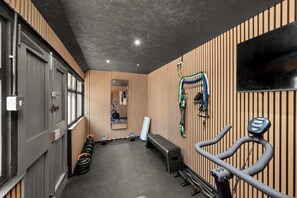 A gym with exercise equipment, a bench, and a television on the wall.
