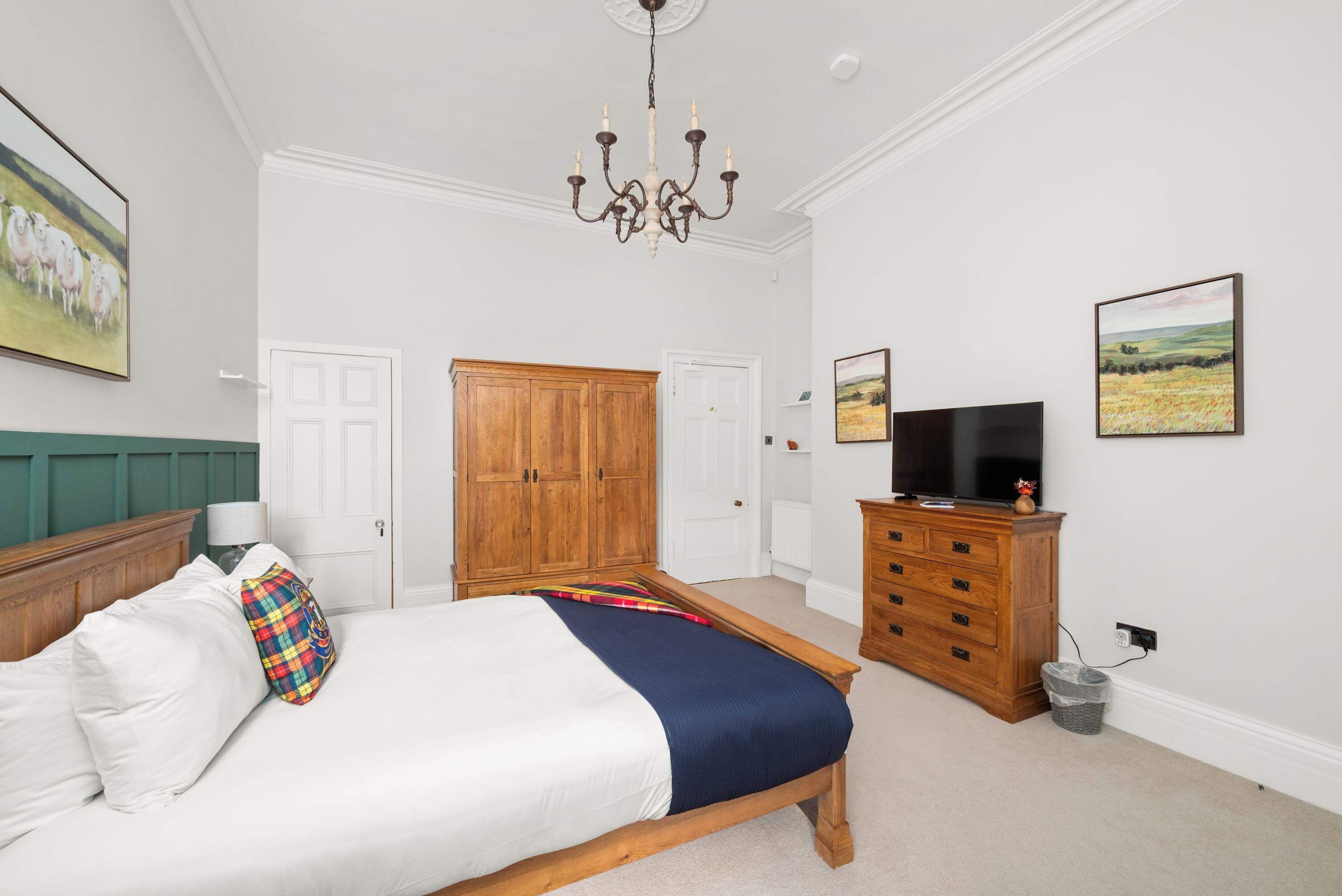 A bedroom with a bed, wooden wardrobe, television, and artwork on the walls.