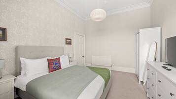 A bedroom with a bed, nightstand, dresser, and a television.