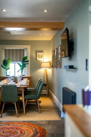 A dining area with a table set for four, chairs, a floor lamp, and a window with blinds.
