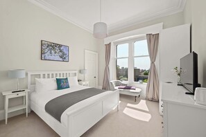 A hotel room with a bed, bedside tables, a desk, a chair, a TV, and a window with curtains.