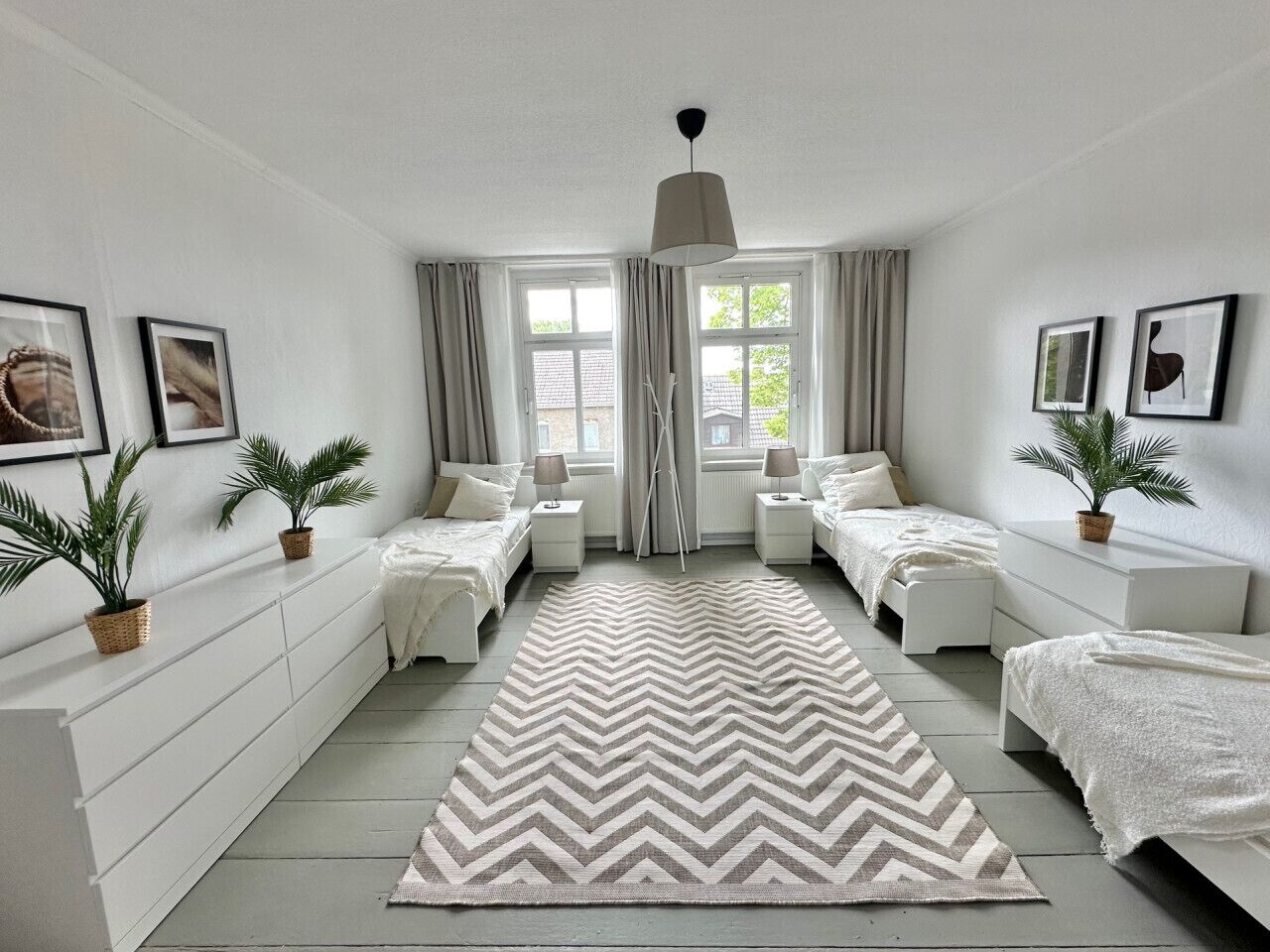 A bedroom with two beds, a large rug, and potted plants.