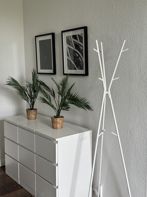 A white dresser with two potted plants, a white coat rack, and two framed pictures on the wall. - Arbio Monteurzimmer Kremmen 6 people (Kremmen)