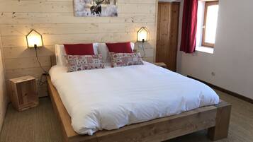 A wooden bed with white bedding, two bedside lamps, a red curtain, and a wall-mounted painting of a deer.