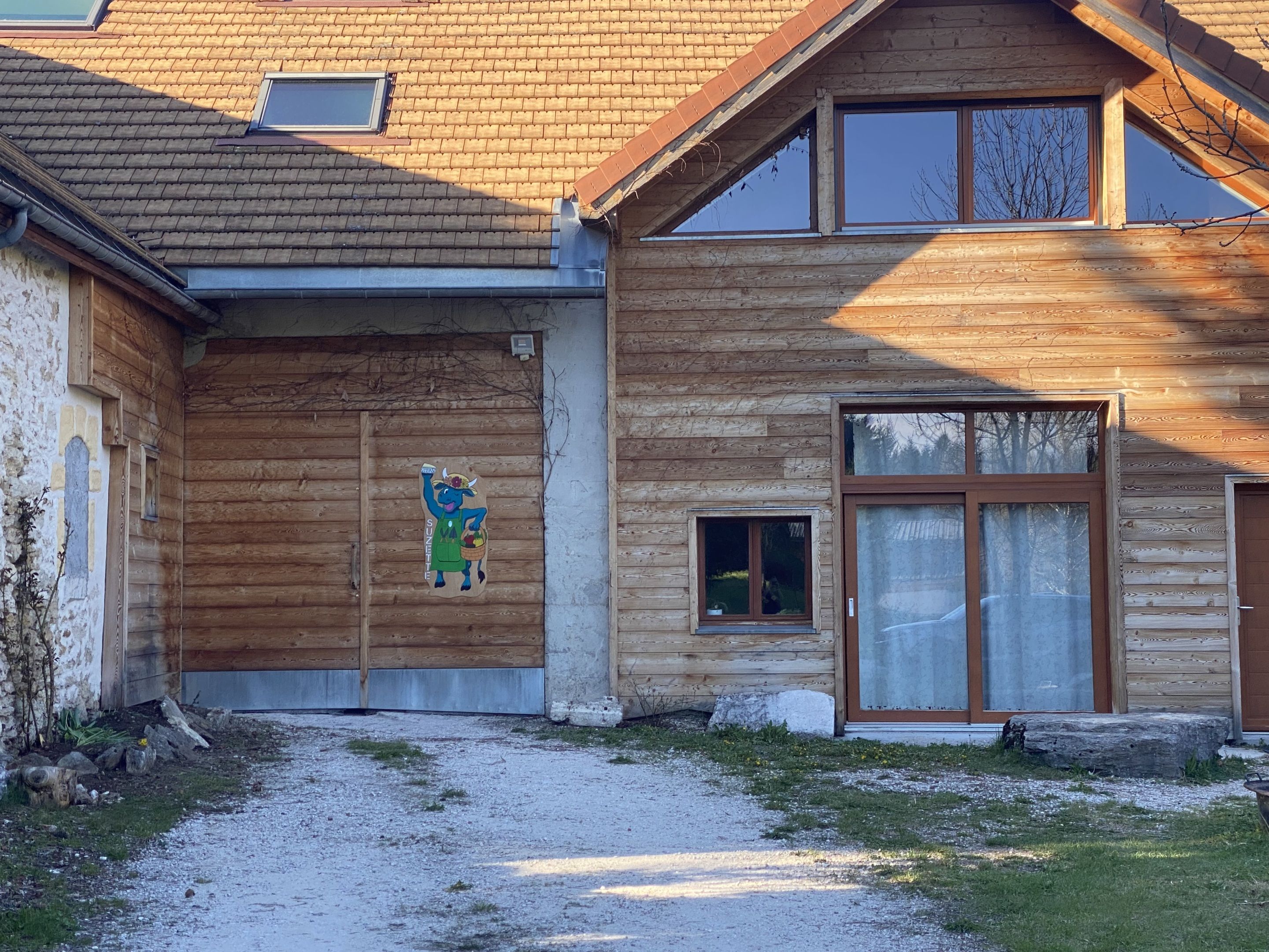 Een houten huis met een groot raam, een kleine deur en een betonnen pad dat naar de ingang leidt.