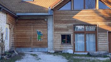 Een houten huis met een groot raam, een kleine deur en een betonnen pad dat naar de ingang leidt.