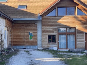 Una casa di legno con un'ampia finestra, una porta piccola e un vialetto in cemento che conduce all'ingresso.