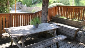 A wooden deck with a bench and a table, surrounded by a wooden fence and greenery.