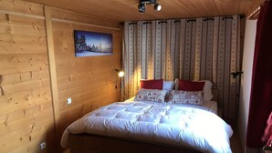 A wooden-paneled room with a bed, a nightstand, a lamp, and a painting on the wall.