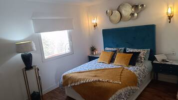 Un dormitorio con cama, mesitas de noche, una lámpara, apliques de pared y una ventana.