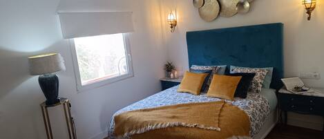 A bedroom with a bed, bedside tables, a lamp, wall sconces, and a window.