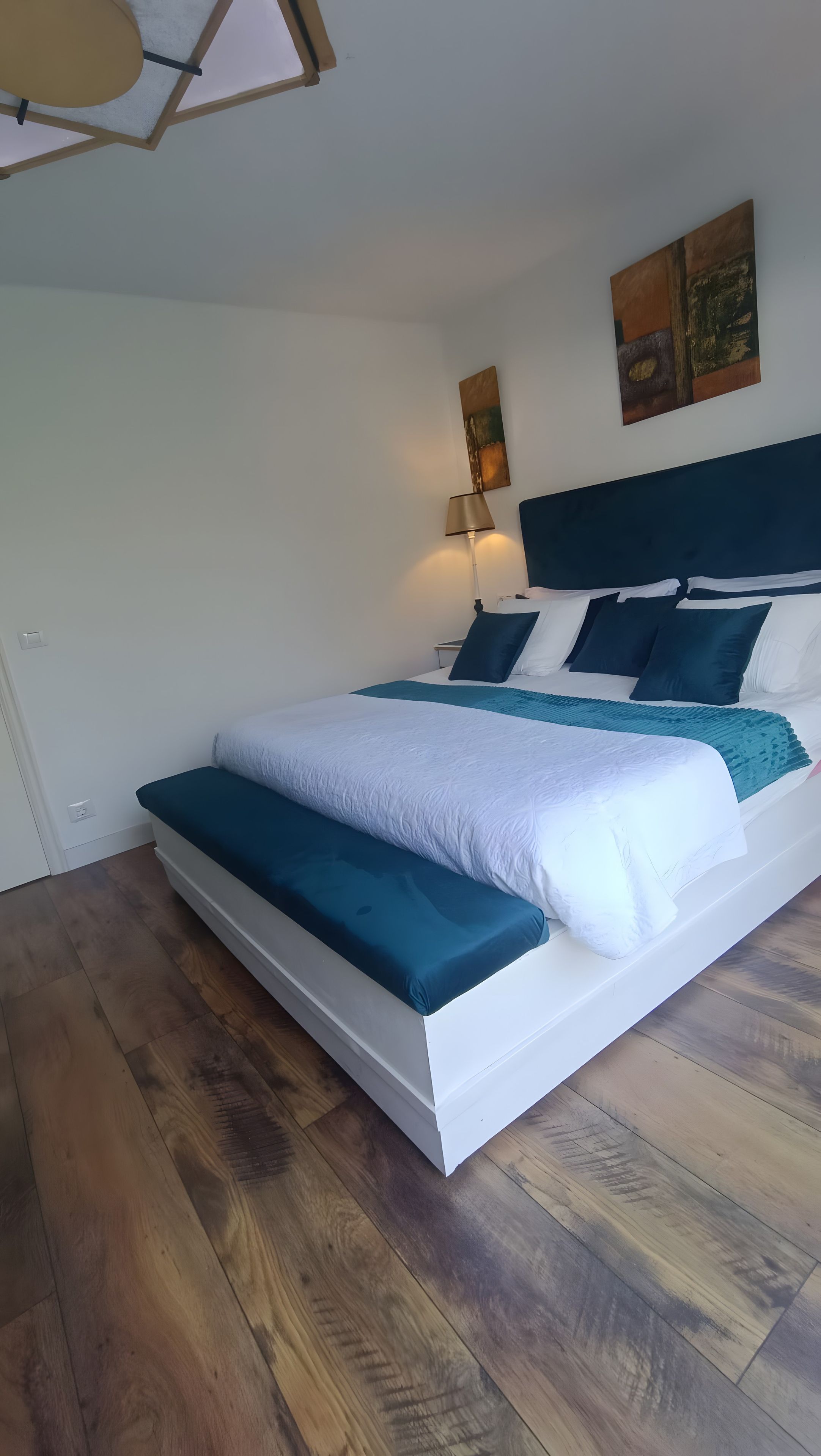 Ein Schlafzimmer mit einem Bett, einer Bank, einer Lampe und Kunstwerken an der Wand.