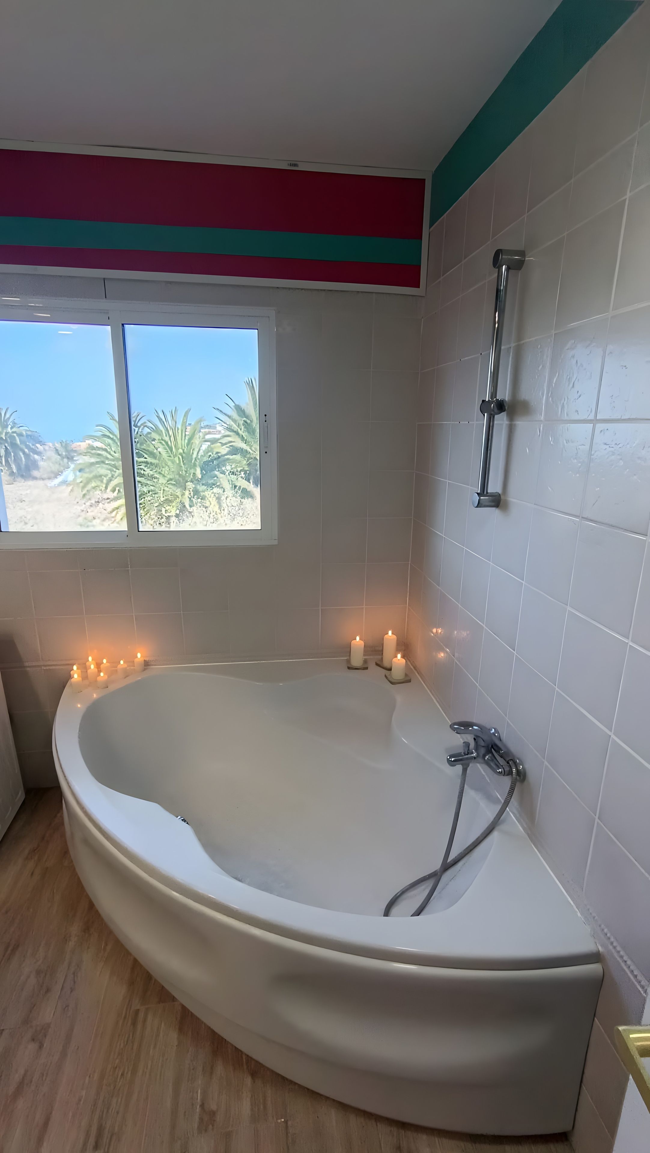 A bathroom with a freestanding bathtub, a window with a view of palm trees, and a shower area.