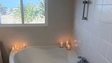 A bathroom with a freestanding bathtub, a window with a view of palm trees, and a shower area.